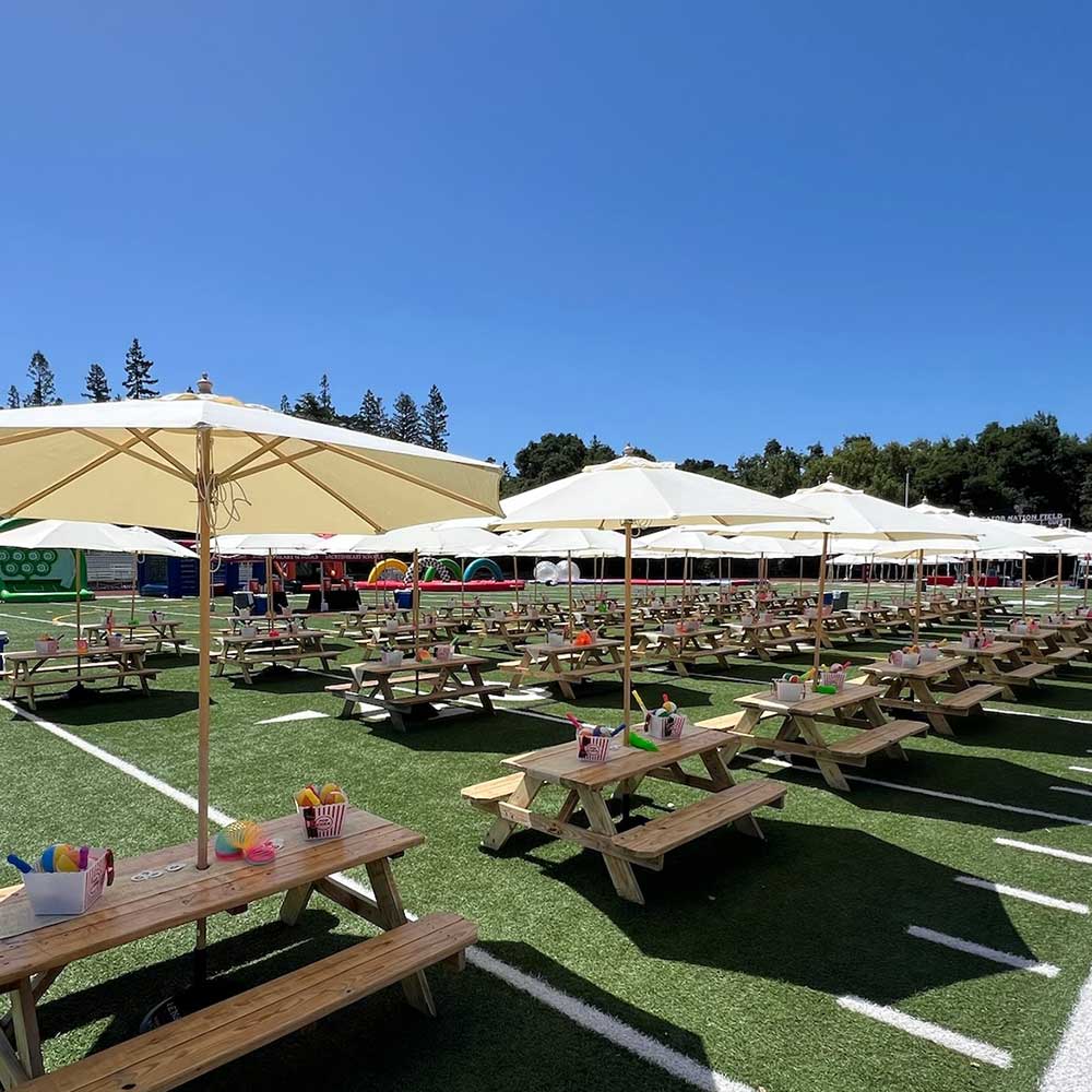 Picnic tables with umbrellas set up on a football field for an outdoor event